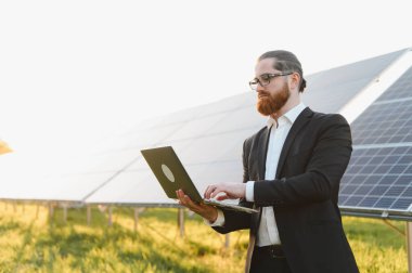 Dizüstü bilgisayar kullanan, güneş enerjisi çiftliğindeki fotovoltaik panelleri yöneten, yenilenebilir enerji ve sürdürülebilir kalkınma yatırımları yapan bir iş adamı