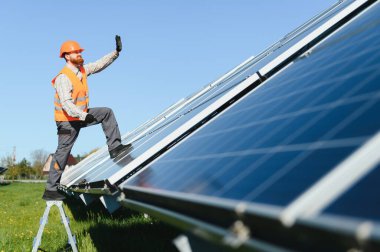 Güneş paneli kurulumunda çalışan güvenlik donanımı giyen teknisyen güneşli bir açık hava ortamında yenilenebilir enerji çözümleri geliştiriyor.
