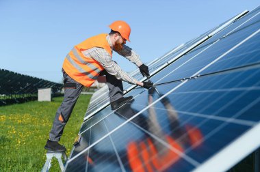 Yenilenebilir ve sürdürülebilir enerji üretimi için büyük bir fotovoltaik fabrikaya güneş panelleri kurulumu üzerinde çalışan erkek teknisyen