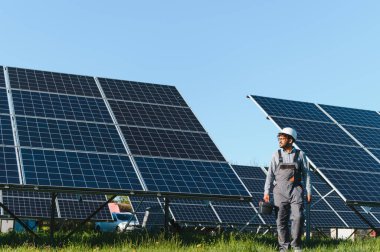 Bir güneş enerjisi santralinde yürüyen orta doğu mühendisi, bir alet çantası taşıyor ve bakım ve kurulum görevlerini denetliyor.