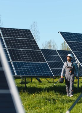 Ortadoğu mühendisi güneşli bir günde güneş panelinde alet çantası taşıyarak yürüyor, teftiş ediyor ve bakım yapıyor.