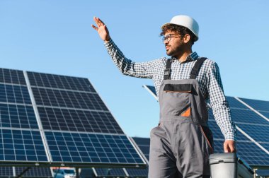 Alet çantası ve başlıklı mühendis, bir enerji santraline güneş panelleri yerleştirirken işaret veriyor