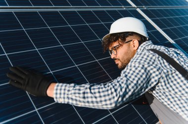 Eldivenli ve kasklı mühendis çatıya güneş paneli yerleştiriyor, sürdürülebilir bir enerji projesi üzerinde çalışıyor.