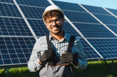 Güvenlik kaskı ve eldiven takarken gülümseyen mühendis, yenilenebilir enerji çözümlerine odaklanmış bir güneş enerjisi santralinde özenle çalışıyor.