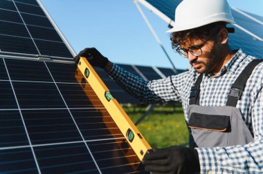 Güneş panelleri kurmak ve yenilenebilir enerji ve sürdürülebilir teknolojiyi vurgulamak için seviye aracı kullanan koruyucu ekipman işçisi