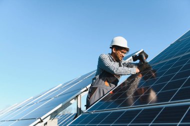 Mühendis bir güneş enerjisi istasyonuna güneş panelleri kurarken yenilenebilir enerji üretimine katkıda bulunan bir elektrikli araç kullanıyor