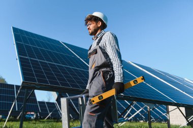 Büyük bir güneş çiftliğinde orta doğu mühendisi bir alet taşıyor ve güneş panellerinin yanında yürüyor.