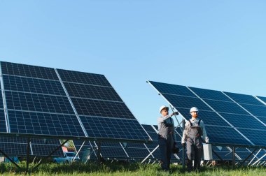 Bir güneş enerjisi santralinde çalışan iki mühendis yenilenebilir enerji üretimi için fotovoltaik paneller kuruyor ve sürdürüyorlar.