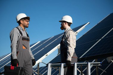 Bir güneş enerjisi santralinde güneş panellerinin kurulumu ve bakımını tartışan mühendisler, yenilenebilir enerji çözümlerine odaklanıyorlar