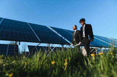 Bir güneş paneli çiftliğinde yürüyen ve denetleyen iki işadamı yenilenebilir enerji ve sürdürülebilirliği tartışıyor.