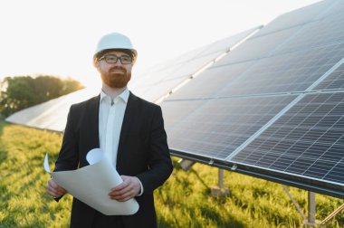 Yatırımcı güneş paneli tarım yatırımlarını gün batımında incelerken elinde planlar tutuyordu.