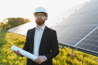 Yeşil bir alanda sürdürülebilir enerji ve yatırım fırsatlarını destekleyen bir güneş paneli kurulumunu denetleyen planlı yatırımcı