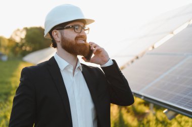 Baş döndürücü bir günbatımında güneş paneli fabrikasını incelerken telefonda konuşan mühendis teknoloji ve doğanın kesişimini vurguluyor.