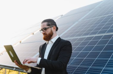 İşadamı yenilenebilir enerji çözümlerine yatırım amaçlı fotovoltaik güneş panellerini değerlendirirken bir dizüstü bilgisayardaki verileri analiz ediyor