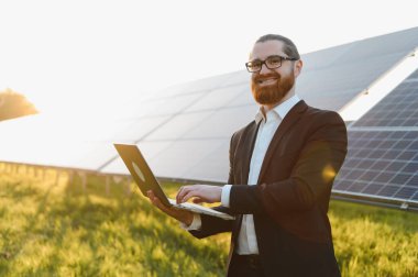 Günbatımında güneş çiftliğindeki fotovoltaik güneş panellerini analiz eden gülen iş adamı, yenilenebilir enerji ve yeşil iş konsepti