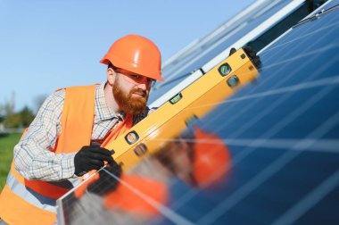 Metal yapı üzerine güneş panelleri kurarken ruh seviyesini kullanan sakallı mühendis, ekolojik yenilenebilir enerji kaynağı üzerinde çalışıyor