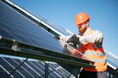 Güneş enerjisi istasyonunda metal kirişlere fotovoltaik paneller yerleştiren tornavidayla çalışan mühendis