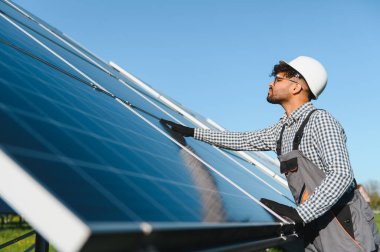 Geniş bir güneş çiftliğinde yenilenebilir enerji ve sürdürülebilirliği destekleyen güneş panelleri kurulumu üzerinde çalışan Ortadoğu mühendisi