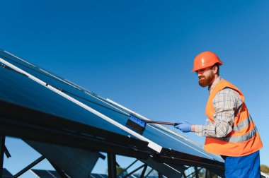Bakım işçisi fotovoltaik panelleri fırçayla temizliyor ve açık mavi gökyüzü altında maksimum enerji üretimini sağlıyor.