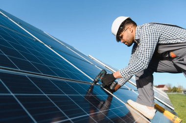 Ekolojik güneş enerjisi santralinde çalışan mühendis, elektrikli tornavida kullanarak fotovoltaik paneller kuruyor.