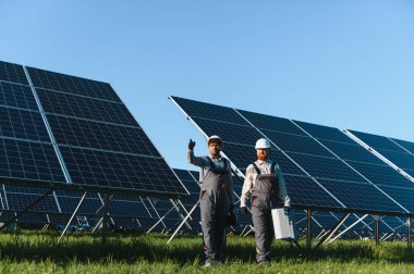 İki mühendis fotovoltaik panelleri kurarken veya tamir ederken bir güneş enerjisi santralinde yürüyen ve taşıyan araçlar