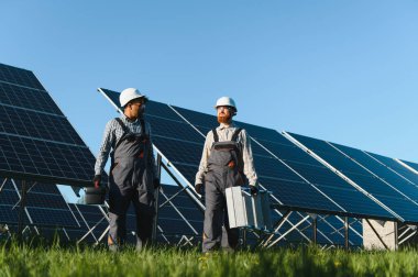 İki teknisyen güneş paneli çiftliğinde yürüyüp araç gereç taşıyorlar, bakım ve onarım operasyonları yapıyorlar.