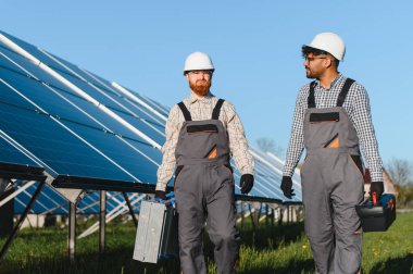 İki çok ırklı mühendis, bir güneş enerjisi santralinde alet çantalarını taşıyarak kurulum ve bakım hakkında tartışıyorlar.