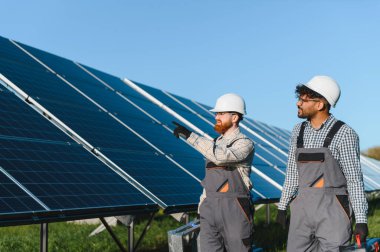 Bir güneş enerjisi santralinde fotovoltaik paneller kurulmasında işbirliği yapan iki mühendis, yenilenebilir enerji çözümlerini teşvik ediyorlar.