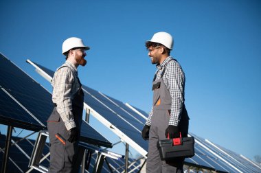 İki çok ırklı mühendis bir güneş enerjisi istasyonuna fotovoltaik paneller montajı sırasında konuşuyor ve gülümsüyor.
