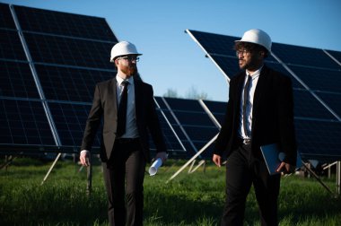 İki çok ırklı mühendis bir güneş enerjisi istasyonundaki fotovoltaik paneller hakkında yürüyor ve tartışıyorlar.