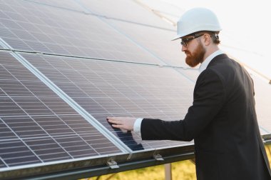Bir güneş çiftliğindeki güneş panellerini inceleyen, sürdürülebilir kalkınma için yenilenebilir enerji çözümlerini değerlendiren takım elbiseli bir yatırımcı.