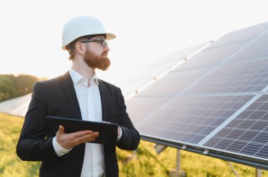 Yatırımcı başlık takıyor, güneş paneli çiftliğini incelerken dijital tablet kullanıyor çarpıcı bir günbatımında, o anın güzelliğini yakalıyor.