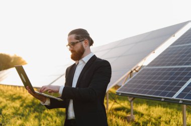 Günbatımında sürdürülebilir bir yenilenebilir enerji santralinde fotovoltaik güneş panellerini analiz eden bir iş adamı
