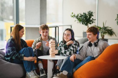 Dört neşeli genç yetişkin puf minderlerinde oturup boş zamanlarının tadını çıkarıyorlar. Tahta blok istifleme oyunu oynuyorlar. Birlikte eğleniyorlar.