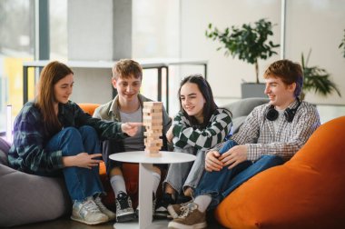 Modern bir çalışma alanında eğlenceli bir istifleme oyununun keyfini çıkaran bir grup genç yetişkin arkadaşça bir rekabete gülüp kaynaşıyorlar.