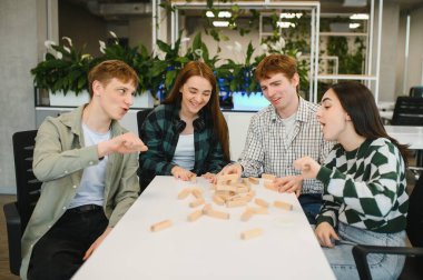 Dört neşeli üniversite öğrencisi, modern bir ofiste ahşap blok oyunu oynarken, mola zamanlarının tadını çıkarıyorlar.