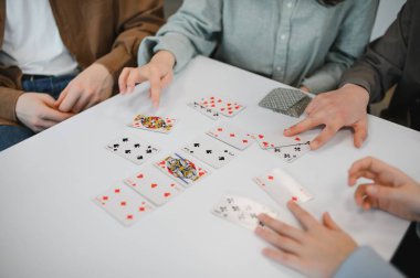 Dostça bir kart oyunu sırasında beyaz bir masada oyun kartları düzenleyen eller, eğlence ve eğlencenin altını çiziyor