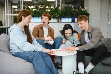 Dört neşeli meslektaşımız, modern ofis ortamında bir masa oyununun tadını çıkarıyor.