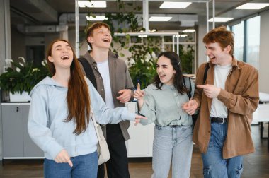 Modern bir üniversite koridorunda dört neşeli öğrenci birlikte yürüyüp gülüyor ve kampüste vakit geçiriyorlar.