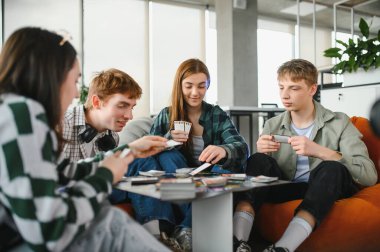 Dört meslektaş, modern ofis ortamında ara verdiklerinde kağıt oynamaktan zevk alarak takım çalışmasını ve arkadaşlığı teşvik ediyorlar.