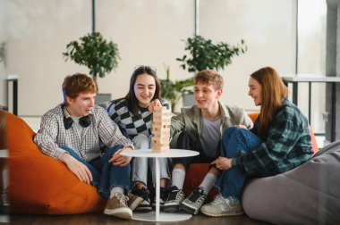 Dört neşeli arkadaş puf minderlerinde oturuyor, arkadaşça bir masa oyunu oynuyorlar, birlikte bir kule inşa ediyorlar ve kahkahalarını paylaşıyorlar.