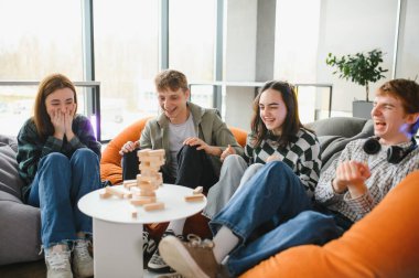 Dört genç yetişkin puf minderlerde otururken bloklama oyunu oynayarak gülüyor ve eğleniyor.