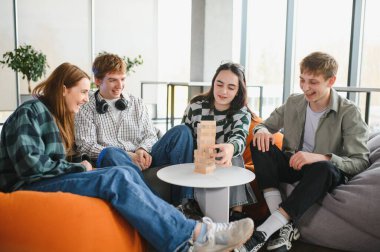 Bir grup genç arkadaş jenga oynuyor, samimi bir ortamda gülüp kaynaşıyorlar. Arkadaşlık ve eğlenceye odaklı rahat ve neşeli bir atmosfer.