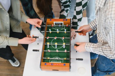 Neşeli genç çalışanlar masa futbolu oynuyorlar, ofiste birlikte eğleniyorlar.