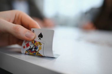 Beyaz bir masada oynanan kart oyununda, karo valesini ortaya çıkaran, rekabetin heyecanını yakalayan el.