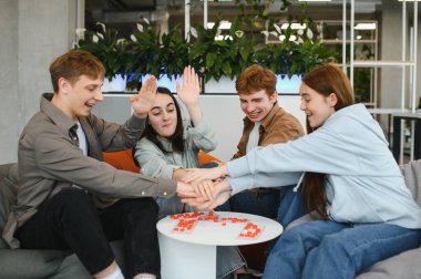 Dört neşeli meslektaşı mola sırasında bir masa oyunundan zevk alıyor, takım çalışması ve dostluk jesti olarak el ele tutuşuyorlar.