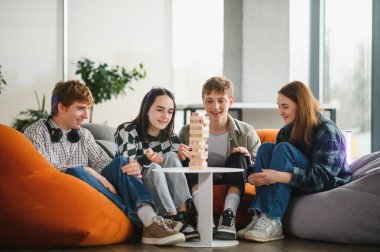 Dört genç arkadaş puf minderlerinde oturmuş, dikkatle bir blok dizme oyunu oynuyor, birlikte vakit geçiriyorlar.