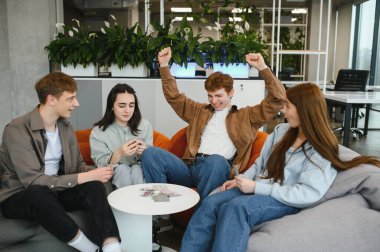 Çağdaş bir ofiste kağıt oyununun keyfini çıkaran dört neşeli meslektaşımız, kazanan eli heyecanla kutluyorlar.