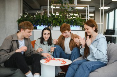 Bir grup genç arkadaş, yeşil ve doğal ışıkla çevrili, modern ve rahat bir ortamda oyun oynuyorlar.