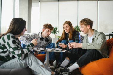 Dört üniversite öğrencisi küçük bir masanın etrafında oturuyor, iskambil oynuyorlar ve üniversitenin dinlenme odasında birlikte eğleniyorlar.